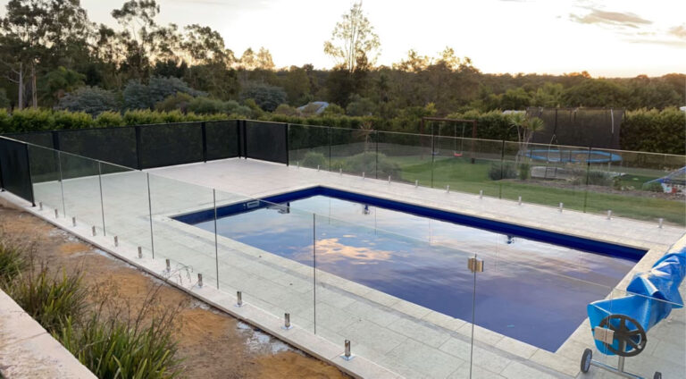 Frameless glass fencing surrounding a deep blue pool at sunset