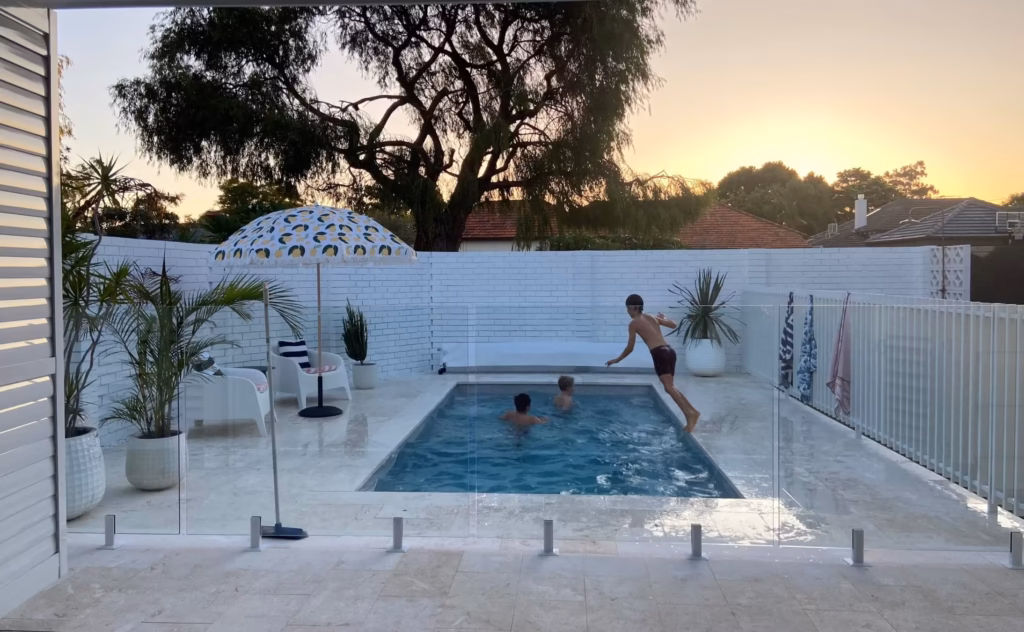 Kids playing in a swimming pool in an outdoor area enclosed by frameless glass and slimline batten fencing
